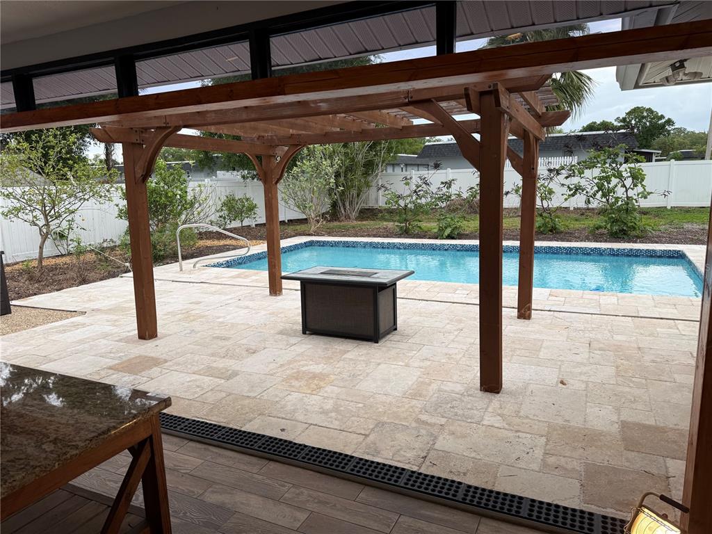 A covered patio features a wooden pergola, stone pavers, and a fire pit overlooking a pool — 98 DADE AVENUE, SARASOTA, FL