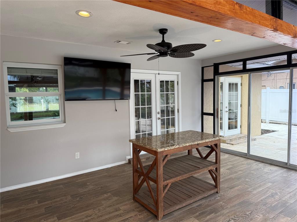 A covered patio features a granite-topped island, a wall-mounted television, and wood-look tile flooring — 98 DADE AVENUE, SARASOTA, FL