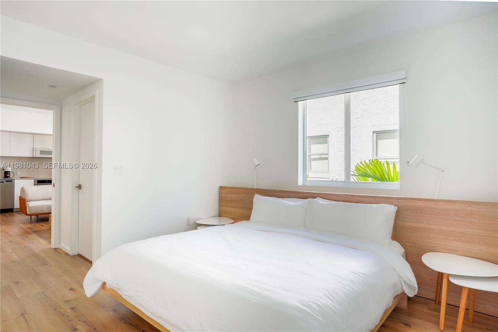 A bedroom features a platform bed with a wood headboard, white bedding, and wood flooring — 136 NE 46th St # 3, Miami FL 33137, MIAMI, FL