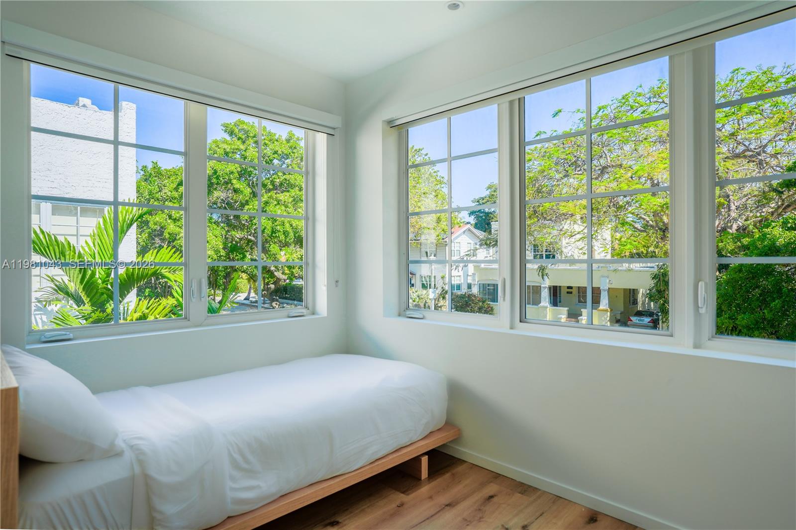 A bedroom with a single bed, light wood flooring, and large windows overlooking trees — 136 NE 46th St # 3, Miami FL 33137, MIAMI, FL