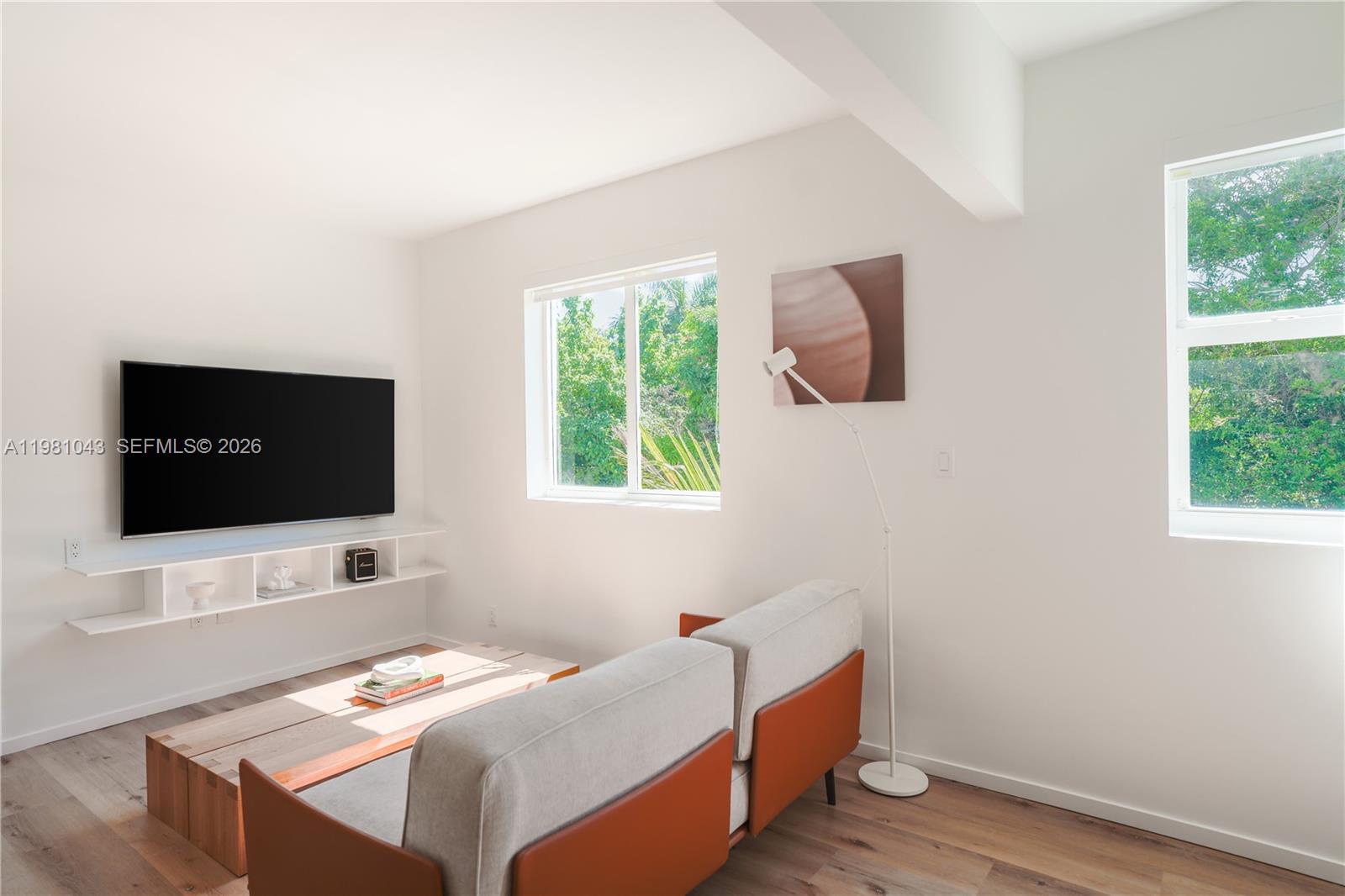 A living room features a wall-mounted television, white shelving, a sofa, and two windows — 136 NE 46th St # 3, Miami FL 33137, MIAMI, FL