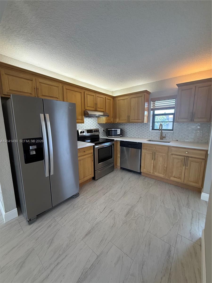 A kitchen features light wood cabinets, stainless steel appliances, white countertops, and tiled flooring — 9273 SW 8th St # 311, Boca Raton FL 33428, BOCA RATON, FL