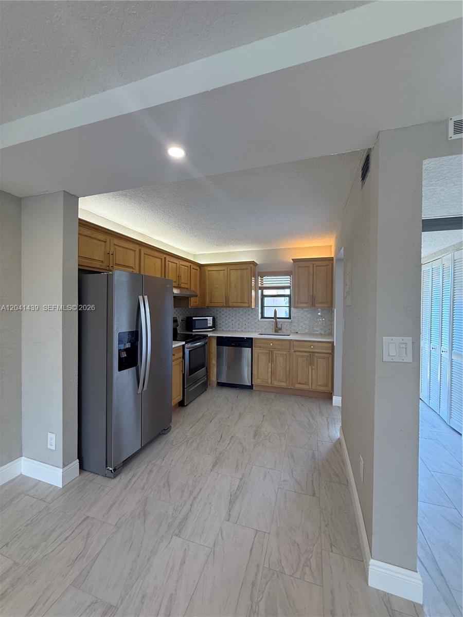A kitchen features light wood cabinets, stainless steel appliances, and light-colored wood-look tile flooring — 9273 SW 8th St # 311, Boca Raton FL 33428, BOCA RATON, FL