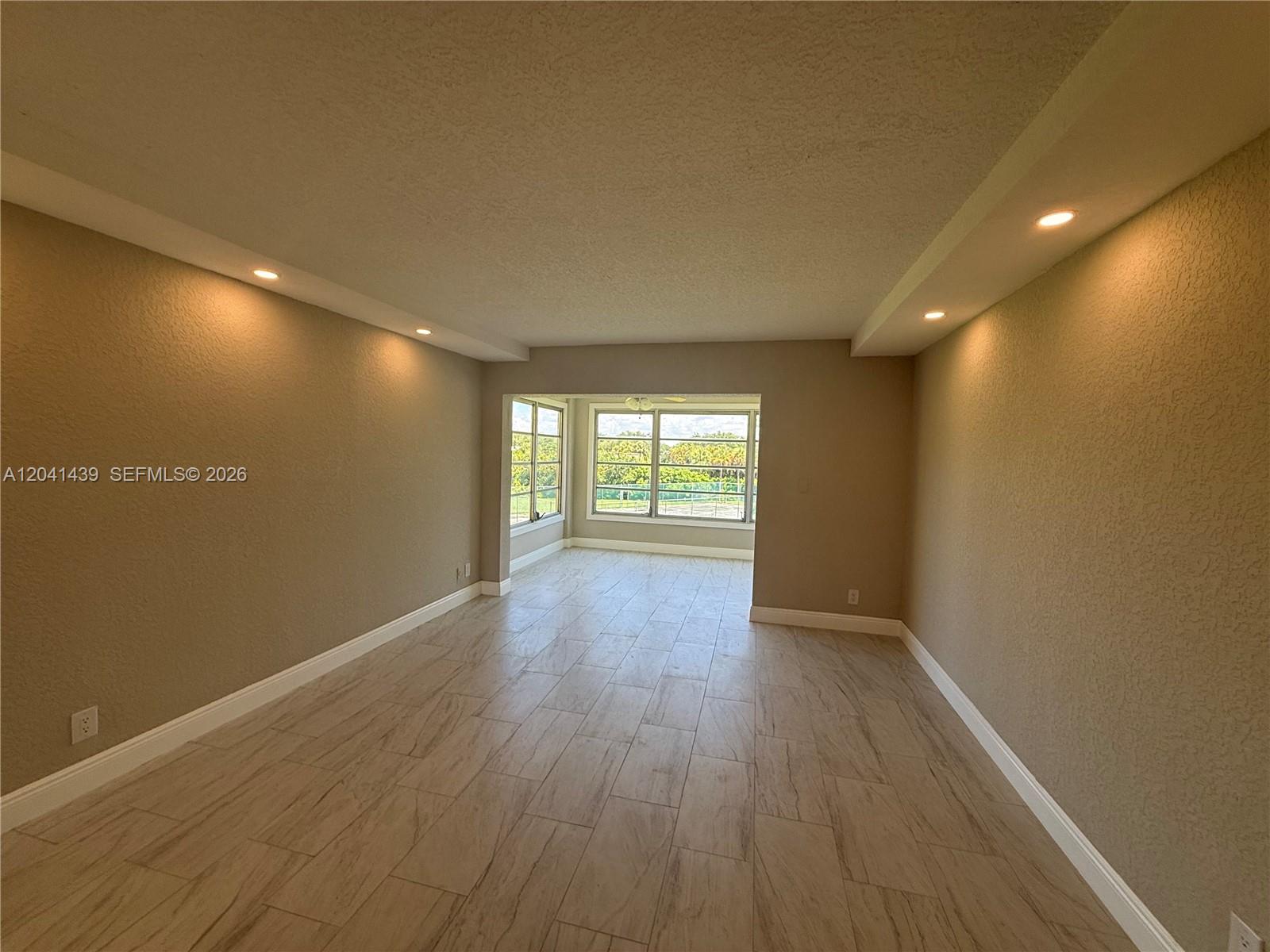An empty room features light-colored wood-look tile flooring, recessed lighting, and large windows — 9273 SW 8th St # 311, Boca Raton FL 33428, BOCA RATON, FL