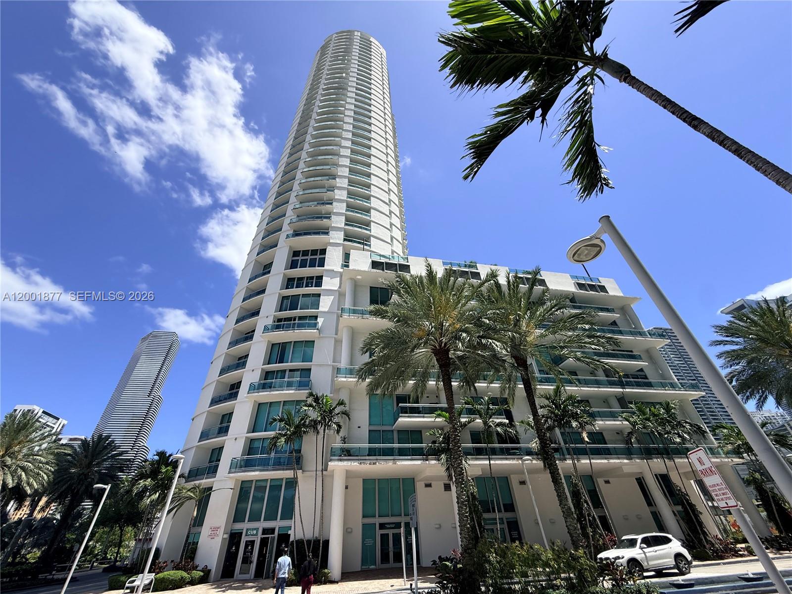 A tall, cylindrical residential skyscraper stands above a multi-story podium with palm trees and landscaping — 350 S Miami Ave # 1601, Miami FL 33130, MIAMI, FL