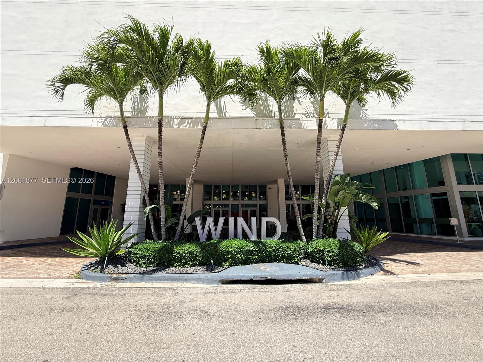 The exterior entrance of a building features palm trees and a large sign reading WIND — 350 S Miami Ave # 1601, Miami FL 33130, MIAMI, FL