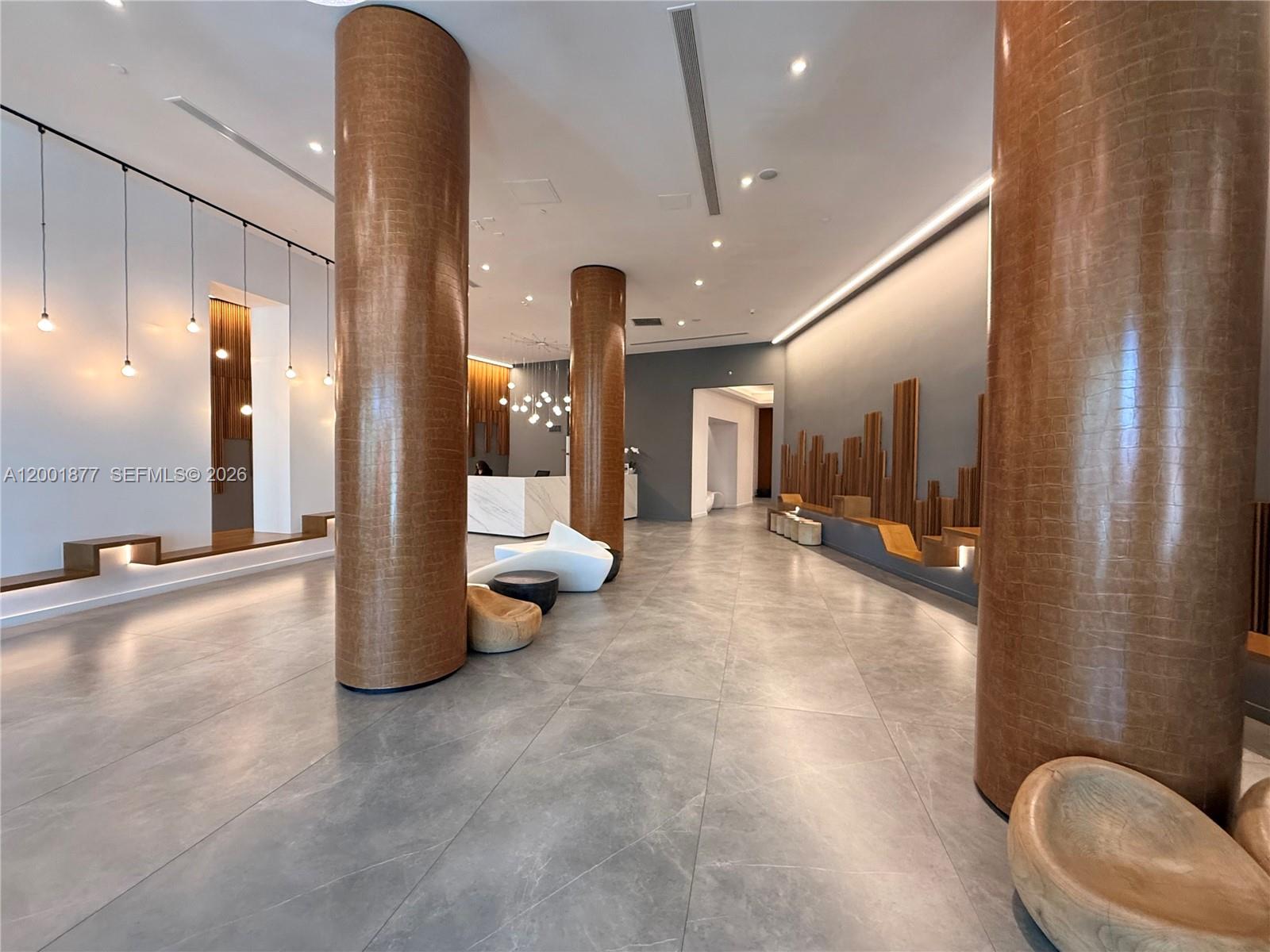 A modern lobby features large textured columns, gray tile flooring, and minimalist seating areas — 350 S Miami Ave # 1601, Miami FL 33130, MIAMI, FL