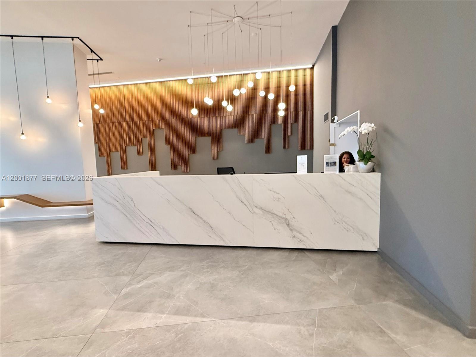 A modern reception area features a marble desk, wood-slat wall paneling, and pendant globe lighting — 350 S Miami Ave # 1601, Miami FL 33130, MIAMI, FL