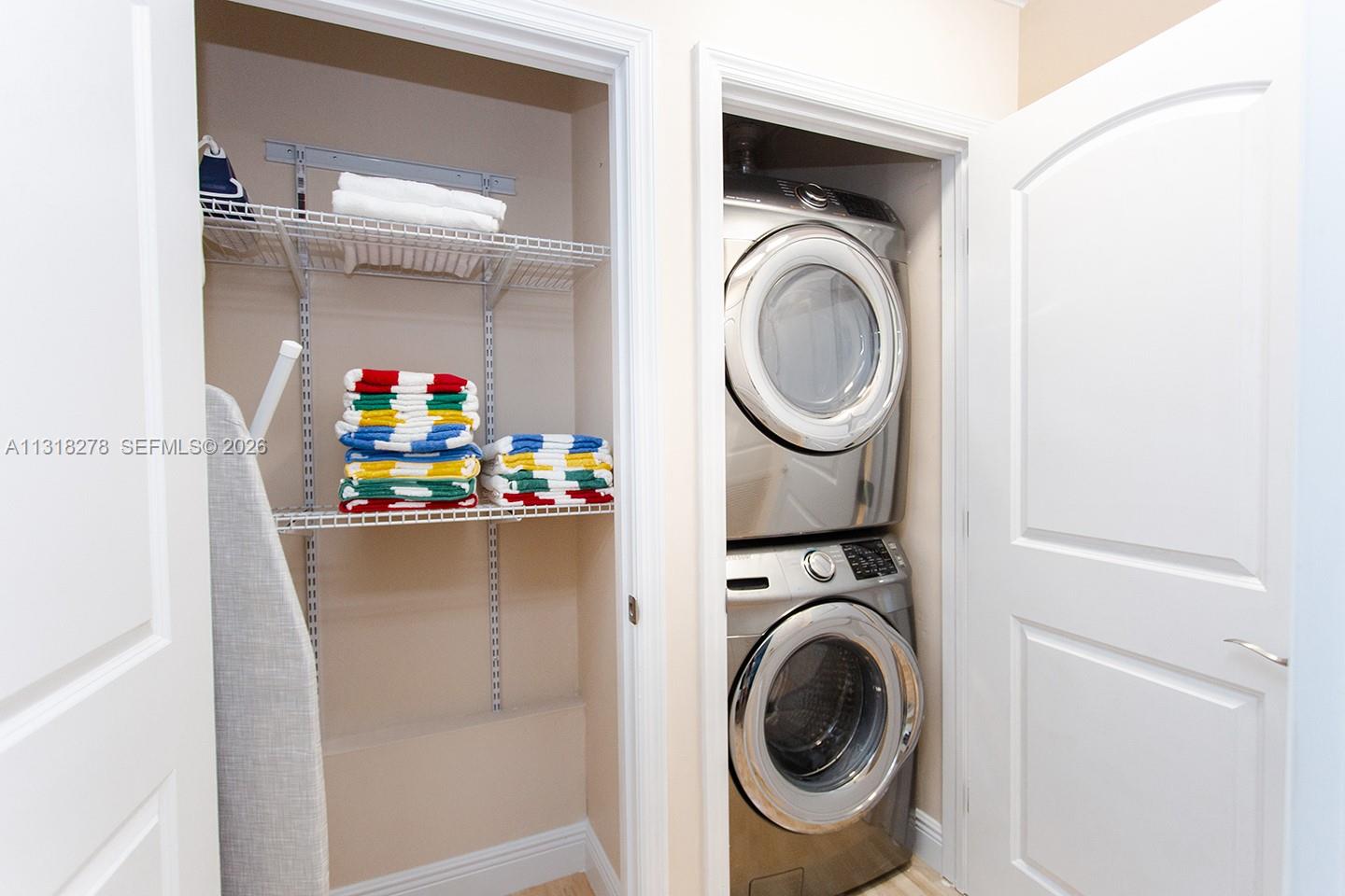 A laundry closet features stacked stainless steel appliances and open wire shelving with folded towels — 825 Harrison St, Hollywood FL 33019, HOLLYWOOD, FL