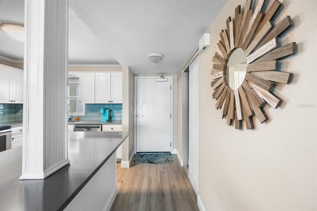 A view of an entryway with light wood flooring, a sunburst mirror, and a kitchen — 1270 GULF BOULEVARD UNIT 606, CLEARWATER BEACH, FL