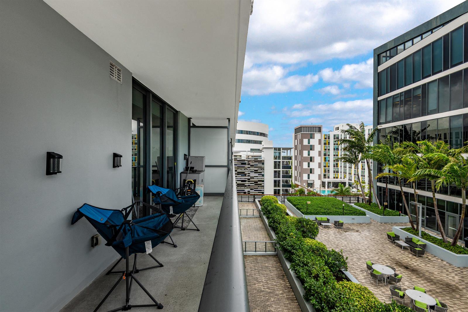 A balcony with two blue folding chairs overlooks a paved courtyard with landscaping and buildings — 2960 NE 207th Street # 708, Aventura FL 33180, AVENTURA, FL