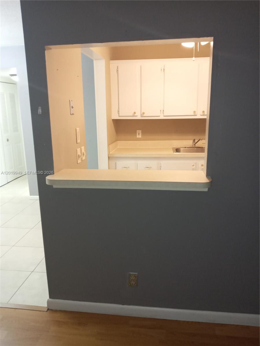 A kitchen with white cabinets and a sink is viewed through a pass-through window — 390 Windsor Q # 390, West Palm Beach FL 33417, WEST PALM BEACH, FL