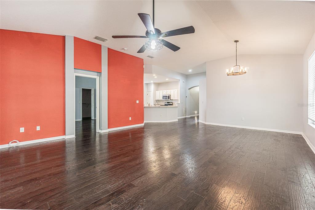 A spacious living room with dark hardwood floors, a vaulted ceiling, and a red accent wall — 19145 WOOD SAGE DRIVE, TAMPA, FL