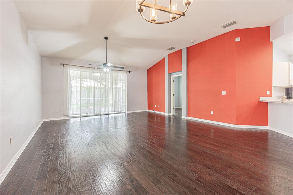 A living room with dark wood floors, a vaulted ceiling, and a bright orange accent wall — 19145 WOOD SAGE DRIVE, TAMPA, FL