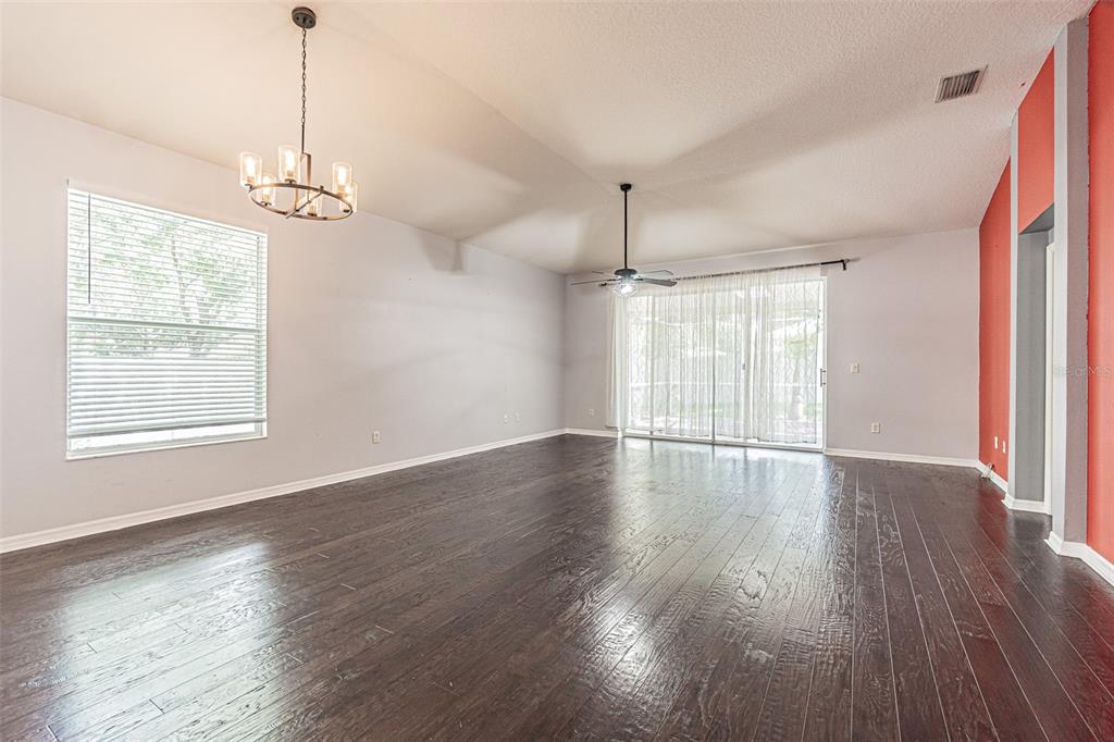 A spacious living room features dark hardwood floors, a chandelier, a ceiling fan, and sliding doors — 19145 WOOD SAGE DRIVE, TAMPA, FL