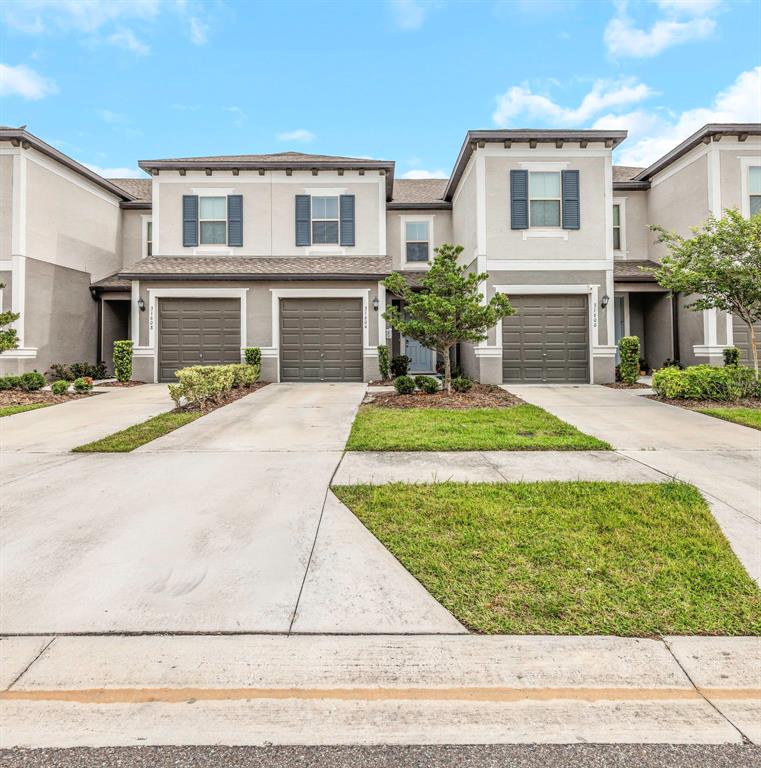 A row of three attached townhomes features beige stucco exteriors, brown garage doors, and driveways — 31604 BLUE PASSING LOOP, WESLEY CHAPEL, FL