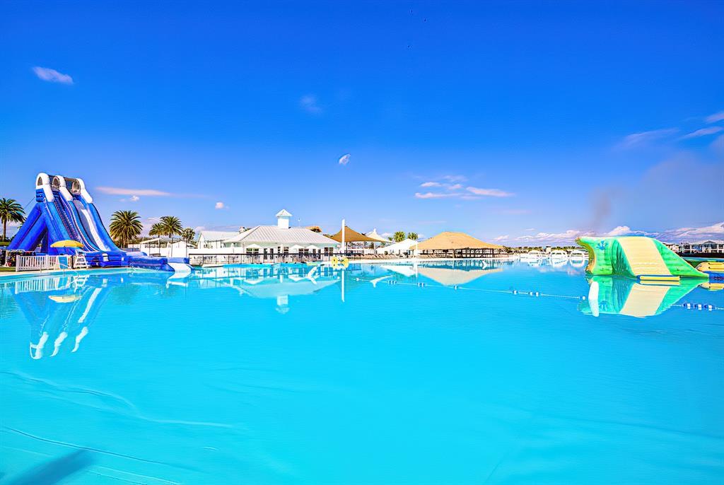 A large, bright blue swimming lagoon features a tall water slide and inflatable obstacles — 31604 BLUE PASSING LOOP, WESLEY CHAPEL, FL