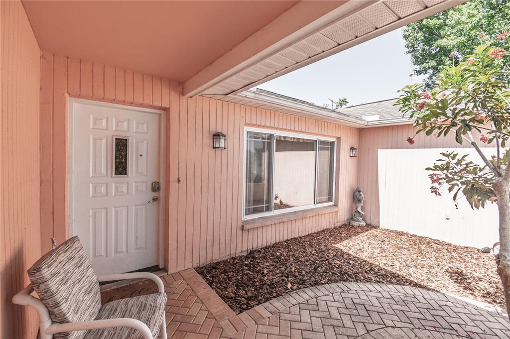 A pink exterior wall with a white front door, a window, and a paved patio area — 7812 TURNBRIDGE DRIVE, PORT RICHEY, FL