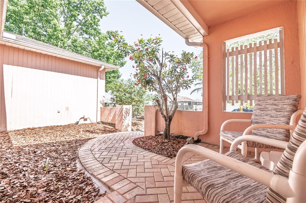 A paved walkway leads to a covered patio with two chairs and a small flowering tree — 7812 TURNBRIDGE DRIVE, PORT RICHEY, FL
