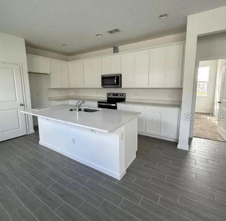 A modern kitchen features white cabinets, a central island, and gray wood-look tile flooring — 4350 DAVOS DRIVE, CLERMONT, FL