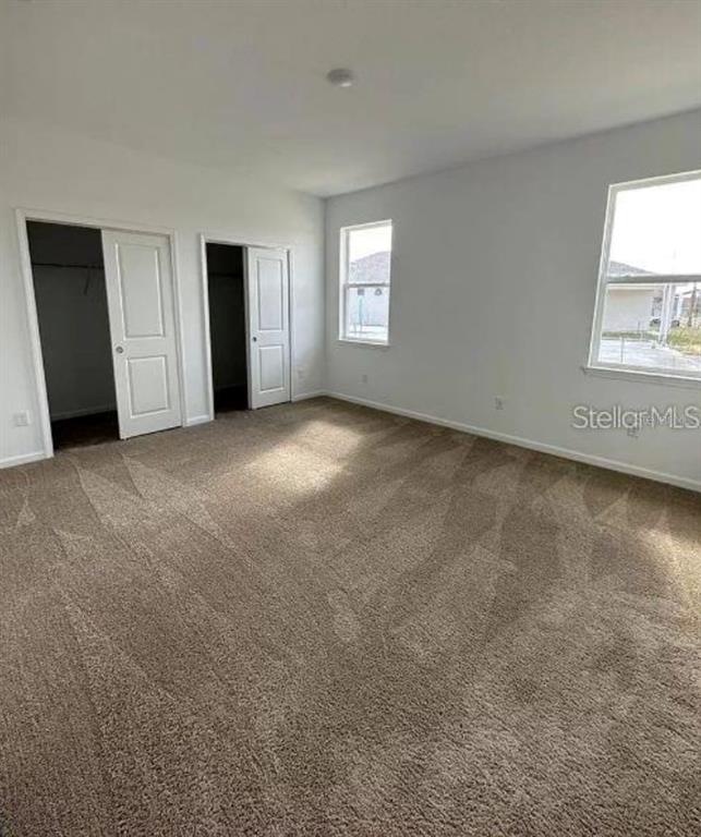 An empty bedroom features beige carpeting, white walls, two closet doors, and two windows — 4350 DAVOS DRIVE, CLERMONT, FL