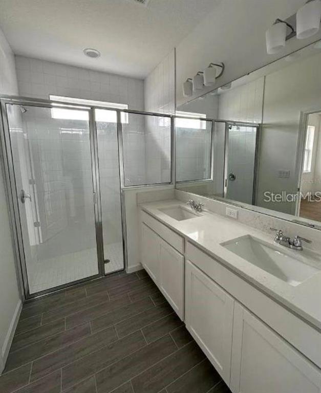 A modern bathroom features a glass-enclosed shower, white vanity with dual sinks, and tile flooring — 4350 DAVOS DRIVE, CLERMONT, FL