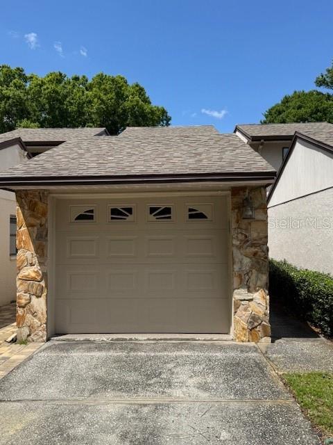 A single-car garage with a tan door and stone veneer siding under a shingled roof — 400 S HOWARD AVENUE, LAKELAND, FL