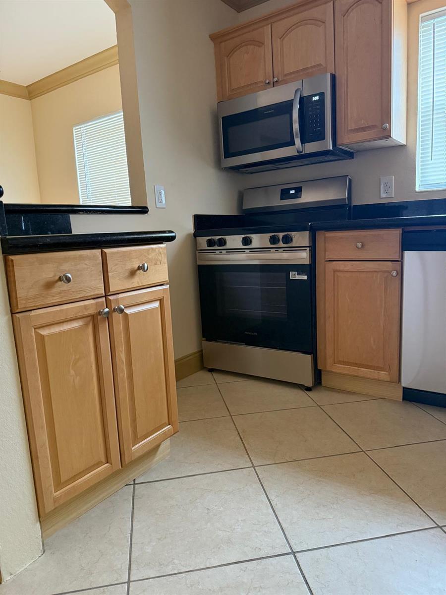 A kitchen features light wood cabinets, black countertops, stainless steel appliances, and beige tile flooring — 744 NE 14th Avenue # 12, Fort Lauderdale FL 33304, FORT LAUDERDALE, FL