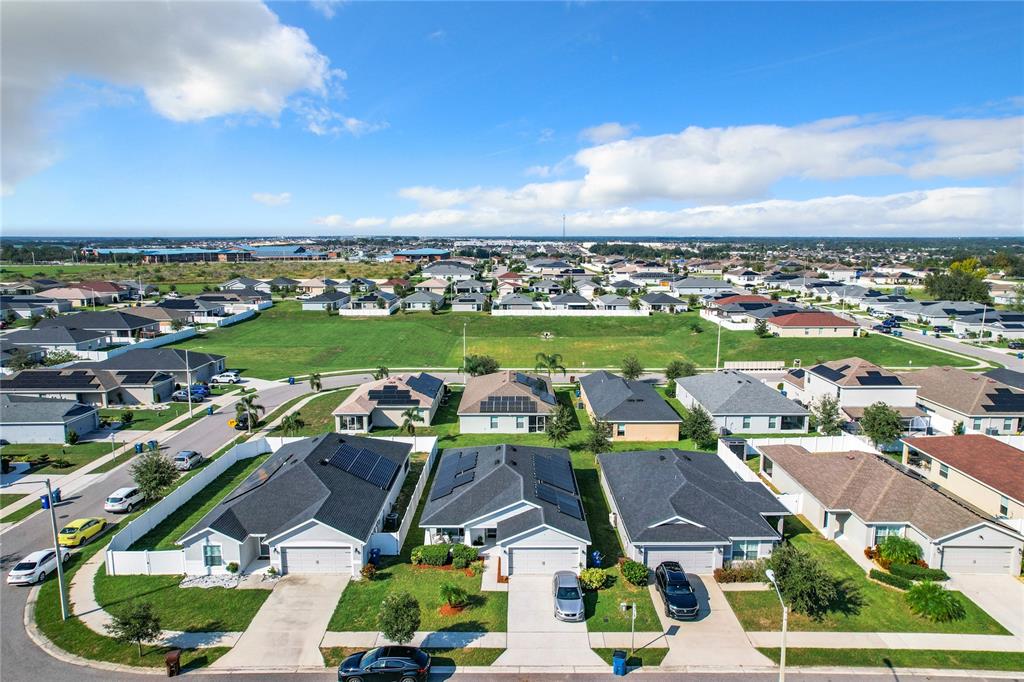 An aerial view shows a suburban neighborhood with single-family homes and a large grassy field — 653 PERSIAN DRIVE, HAINES CITY, FL
