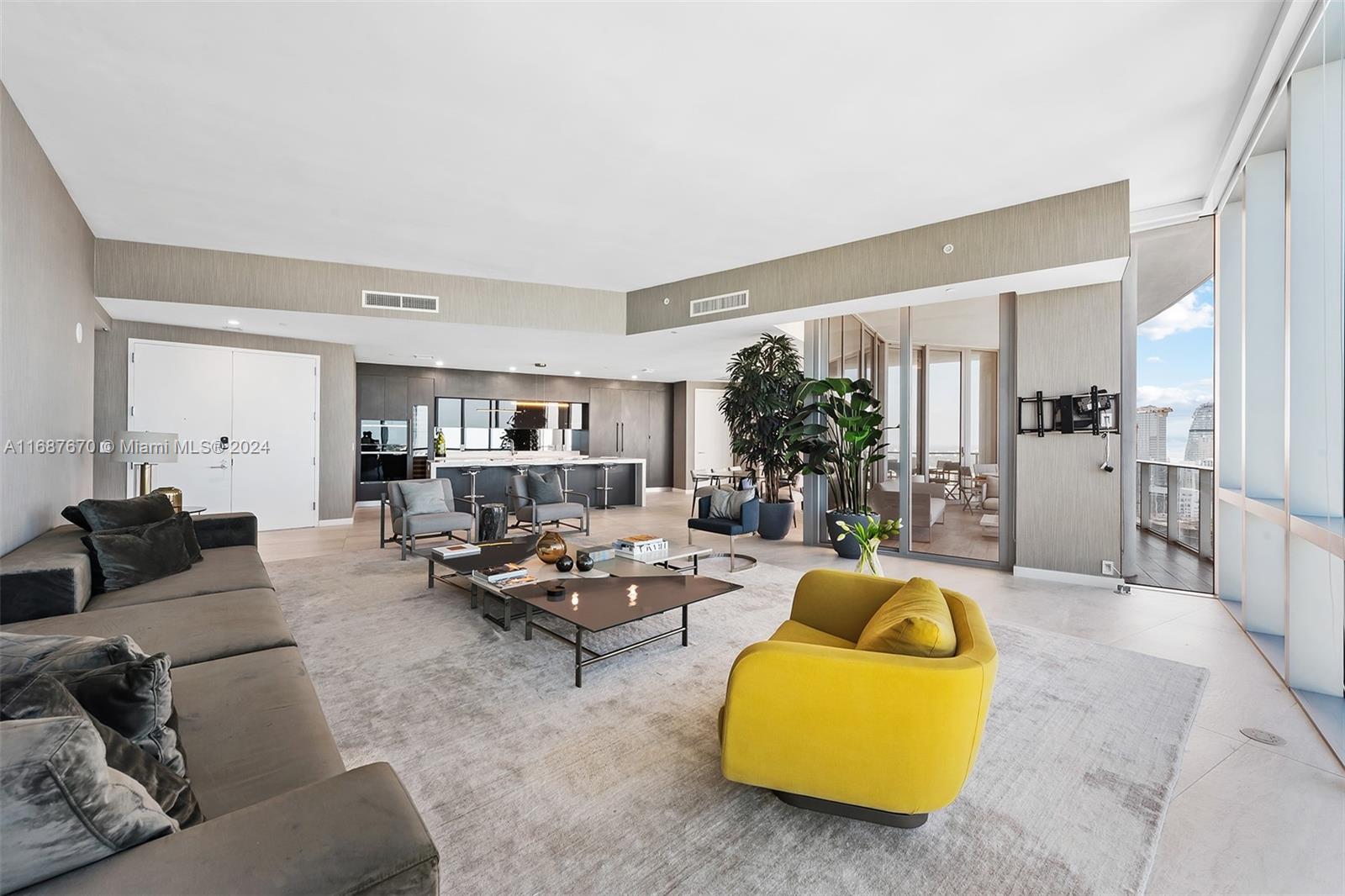 A modern open-concept living room features a grey sectional, yellow armchair, and a kitchen area — 851 NE 1st Ave # 5112, Miami FL 33132, MIAMI, FL
