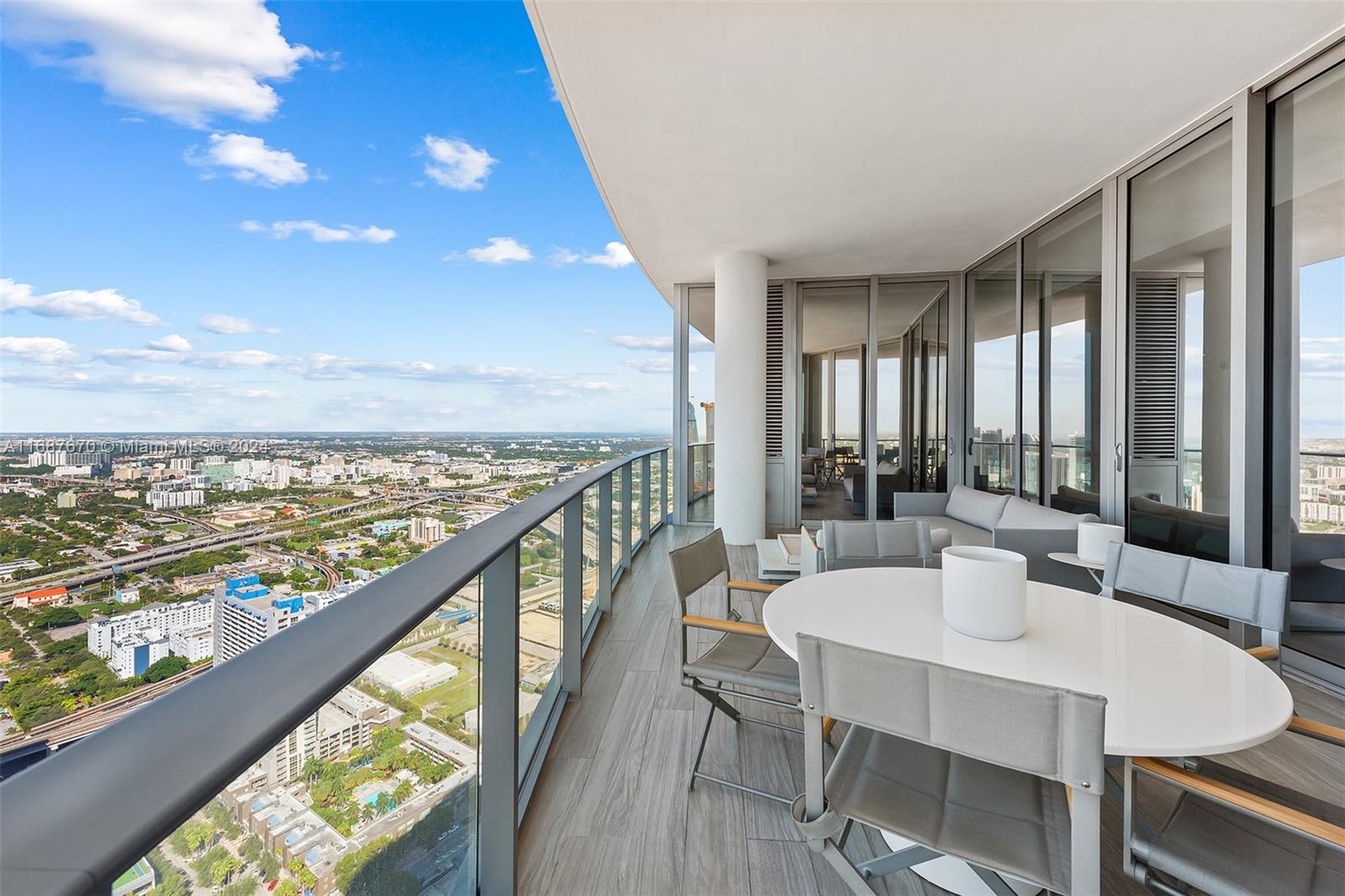 A high-rise balcony features a dining set, outdoor seating, and panoramic city views — 851 NE 1st Ave # 5112, Miami FL 33132, MIAMI, FL