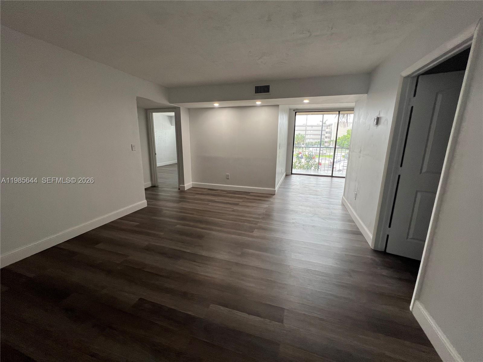 An empty room features dark wood-look flooring, white walls, recessed lighting, and a sliding glass door — 8635 NW 8th St # 211, Miami FL 33126, MIAMI, FL