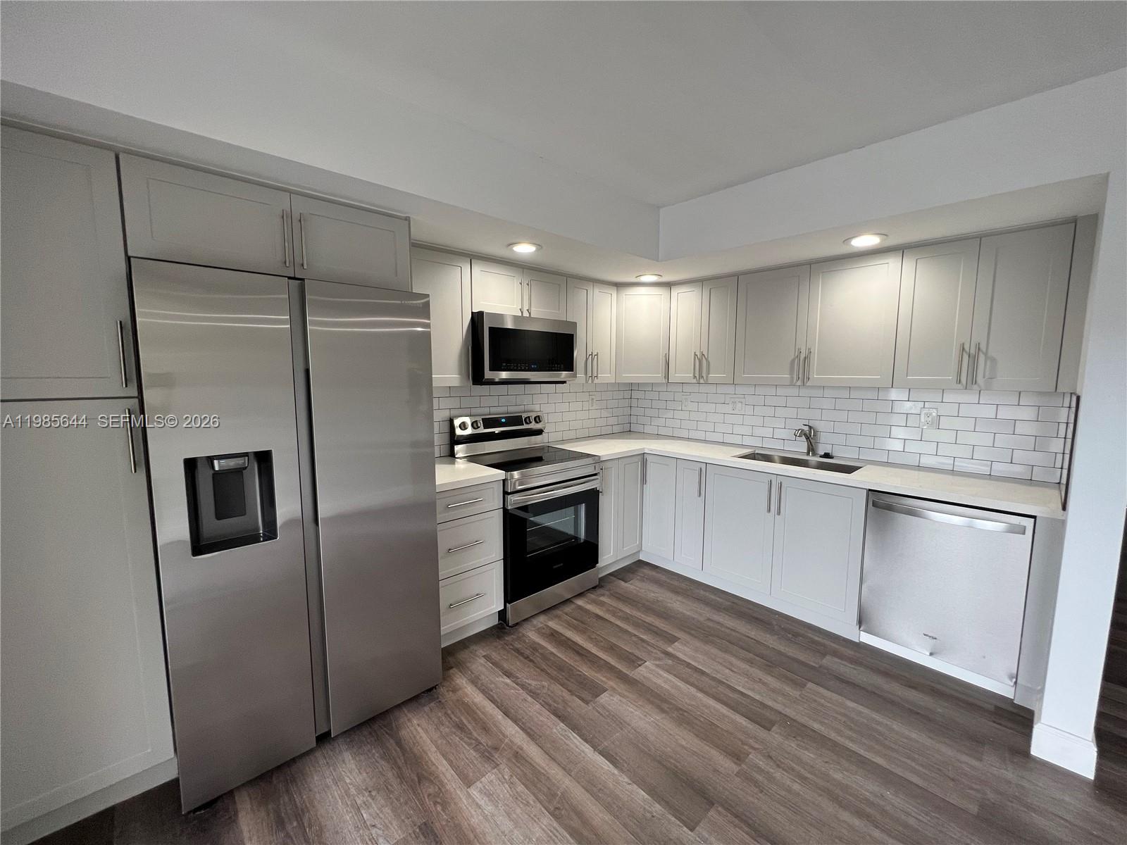 A modern kitchen features gray cabinets, stainless steel appliances, white countertops, and subway tile backsplash — 8635 NW 8th St # 211, Miami FL 33126, MIAMI, FL