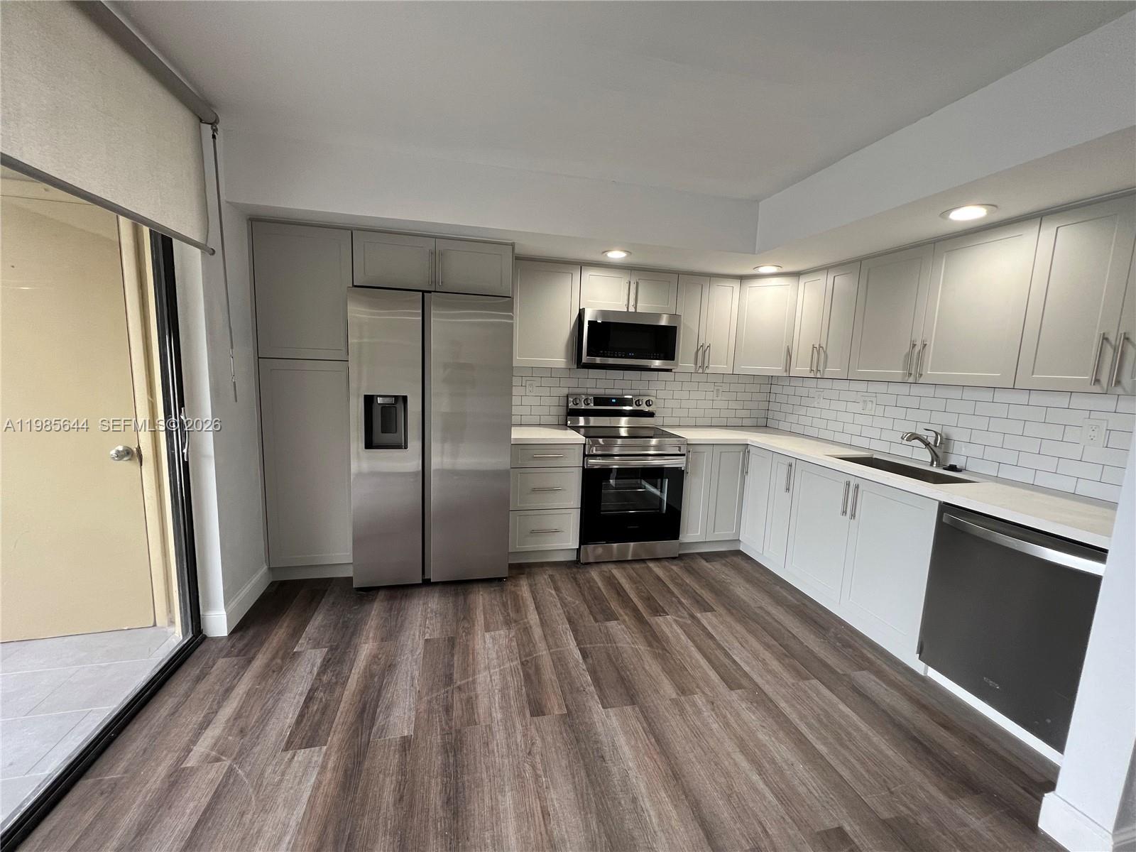 A kitchen features light gray cabinets, stainless steel appliances, white countertops, and wood-look flooring — 8635 NW 8th St # 211, Miami FL 33126, MIAMI, FL