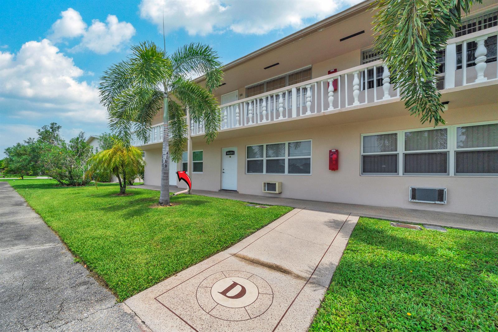 A two-story apartment building exterior features a concrete walkway with a letter D emblem — 49 Hastings # D, West Palm Beach FL 33417, WEST PALM BEACH, FL