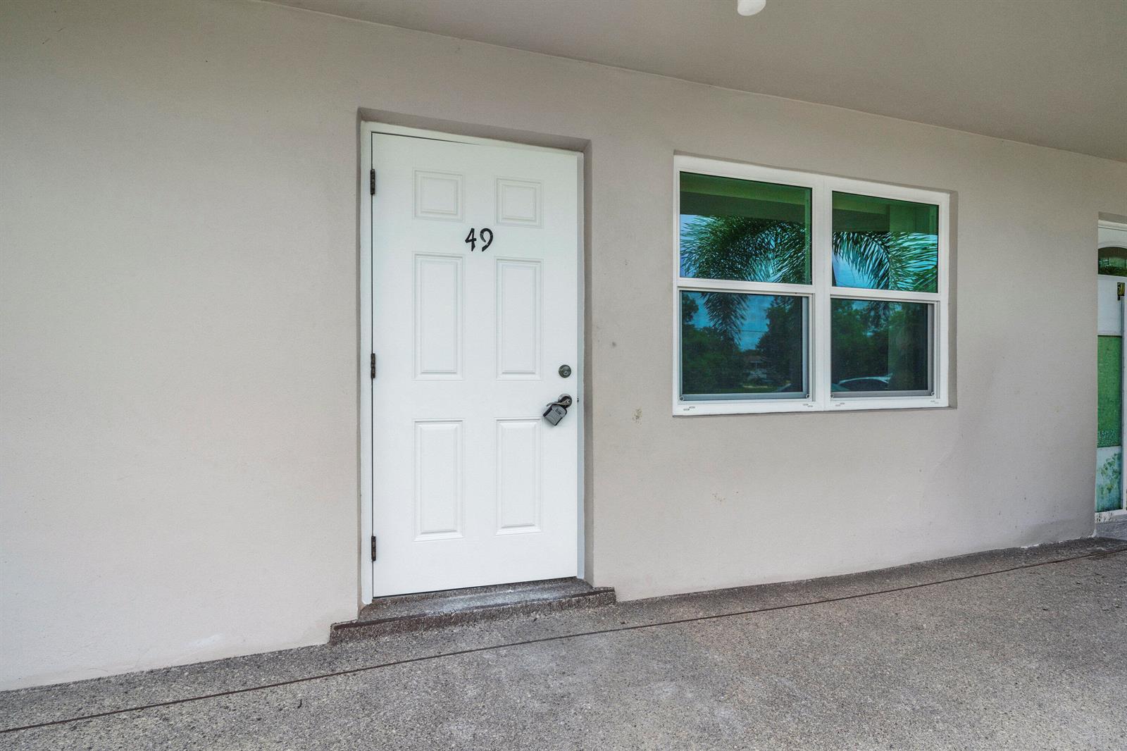 A white exterior door numbered 49 sits next to a window on a concrete walkway — 49 Hastings # D, West Palm Beach FL 33417, WEST PALM BEACH, FL