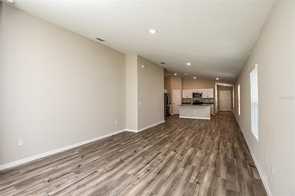 An open-concept living area features wood-look flooring, recessed lighting, and a kitchen in the background — 4531 WYNNSTONE DRIVE, DAVENPORT, FL