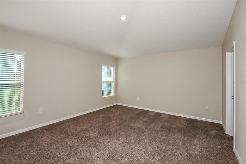 An empty bedroom with beige walls, brown carpet, two windows with blinds, and a doorway — 4531 WYNNSTONE DRIVE, DAVENPORT, FL