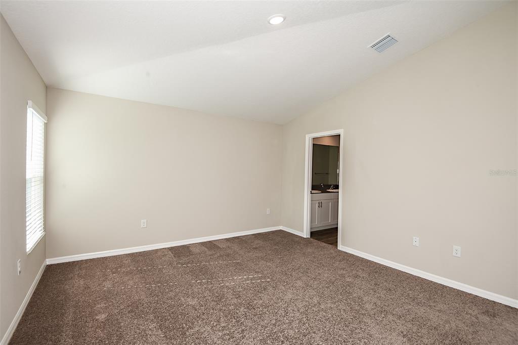 A carpeted bedroom with beige walls, a window, and a doorway leading to a bathroom — 4531 WYNNSTONE DRIVE, DAVENPORT, FL