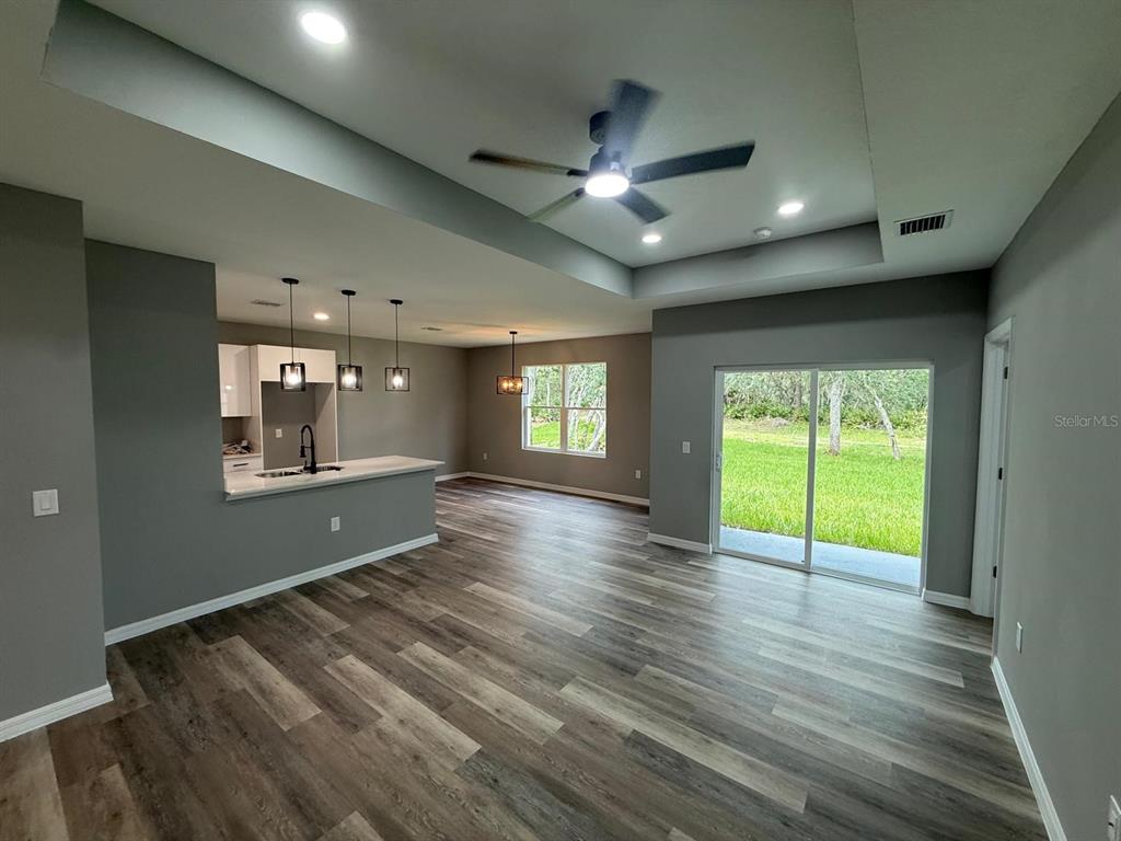 An open-concept living area features a kitchen with pendant lights, wood-look flooring, and sliding doors — 1627 PICKEREL COURT, POINCIANA, FL