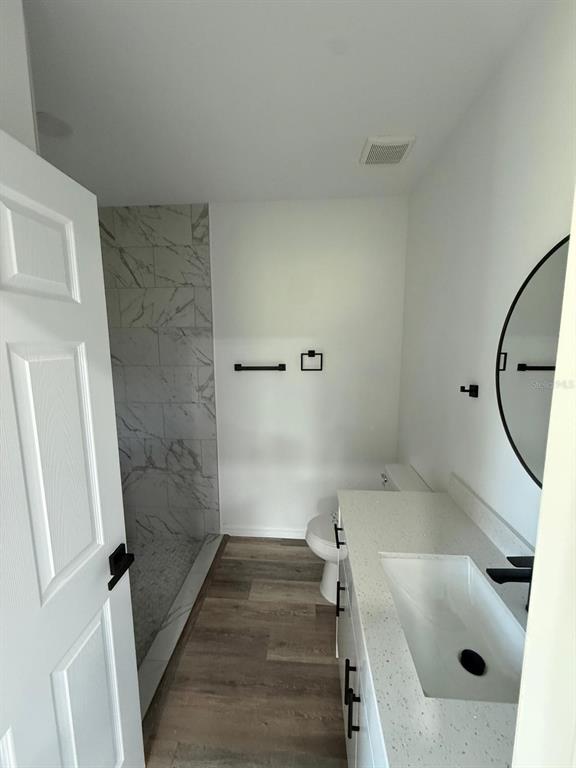 A modern bathroom features a marble-tiled walk-in shower, wood-look flooring, and a white vanity — 1627 PICKEREL COURT, POINCIANA, FL