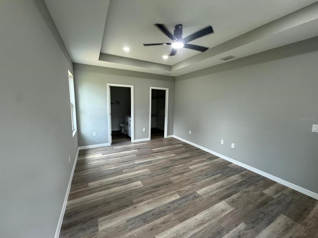 A bedroom with gray walls, wood-look flooring, a tray ceiling, and two doorways — 1627 PICKEREL COURT, POINCIANA, FL