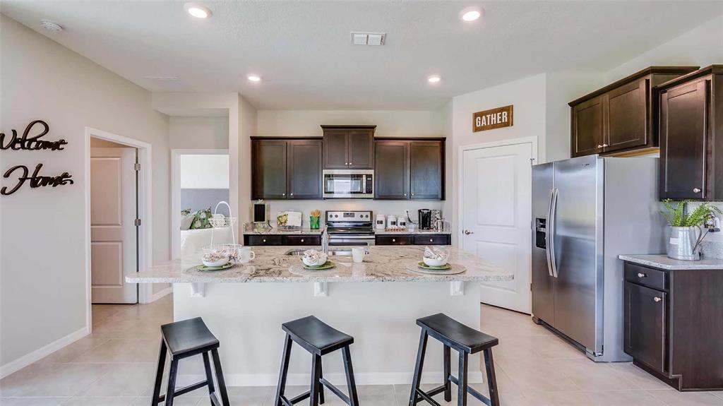 A kitchen features dark wood cabinets, granite countertops, a central island, and stainless steel appliances — 4346 FENCE ROW COURT, LAKEWOOD RANCH, FL