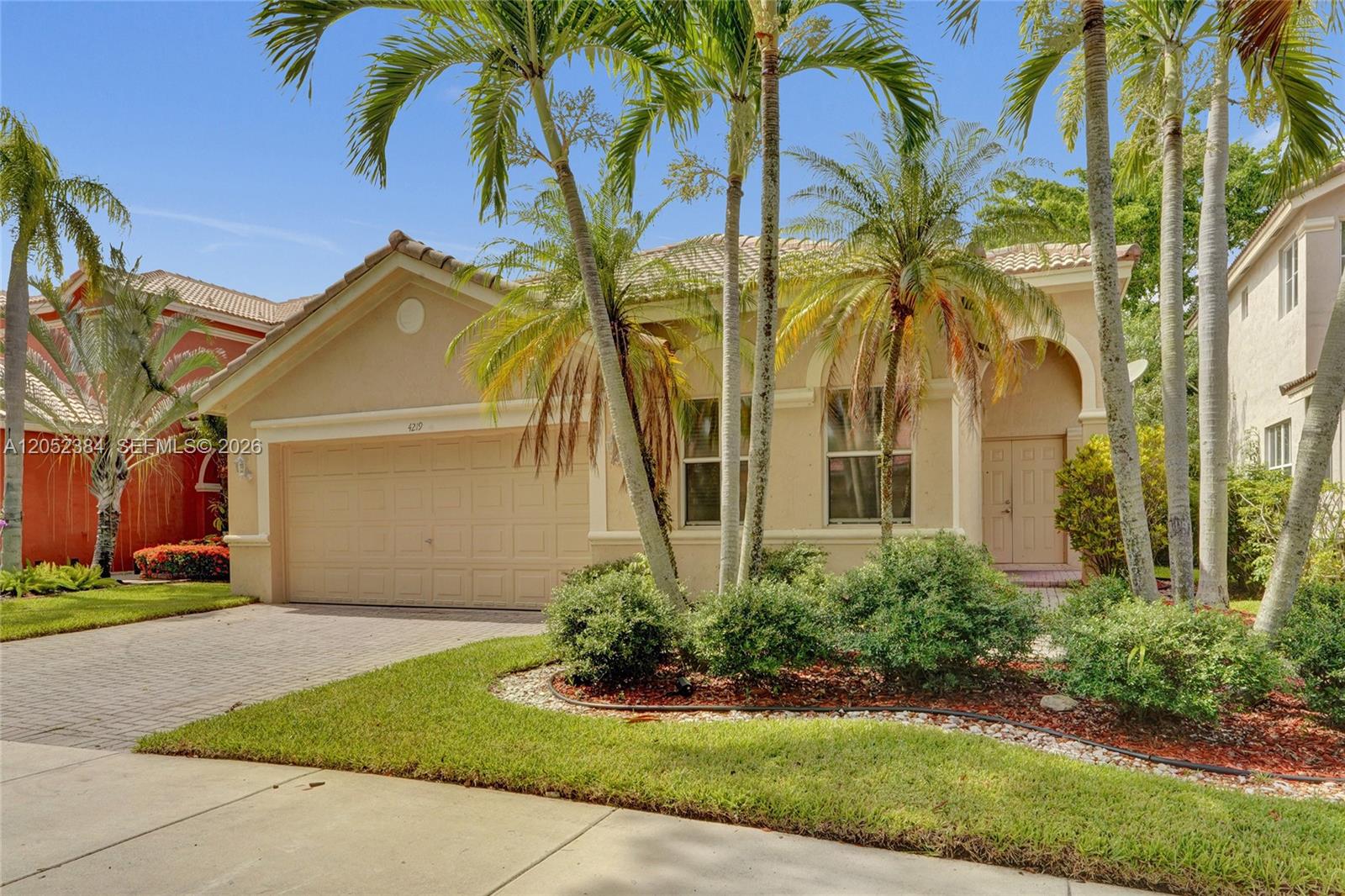 A tan single-story house with a two-car garage and palm trees in the front yard — 4219 Sabal Ridge Cir, Weston FL 33331, WESTON, FL