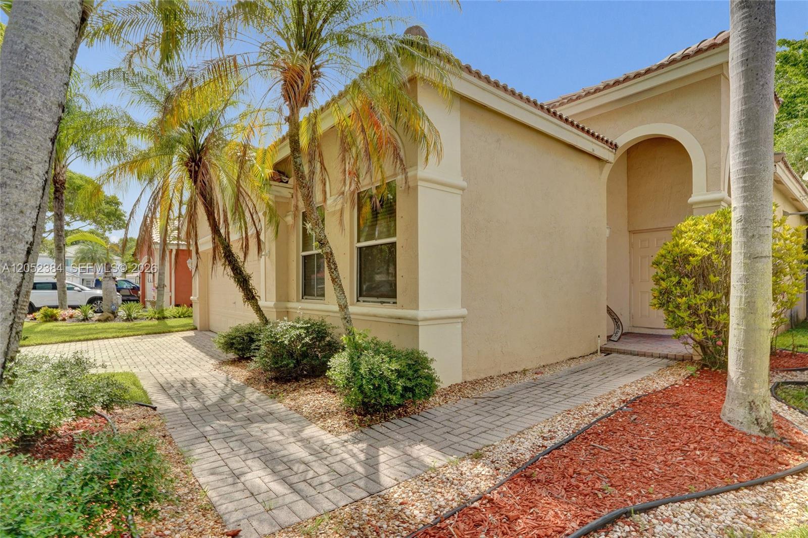 A beige stucco house features a brick paver walkway, palm trees, and a covered entryway — 4219 Sabal Ridge Cir, Weston FL 33331, WESTON, FL