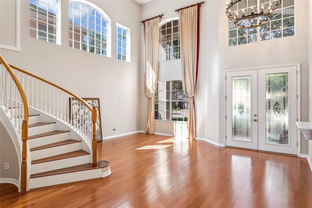 A bright foyer features hardwood floors, a curved staircase, and tall windows with floor-length curtains — 10226 DEERCLIFF DRIVE, TAMPA, FL