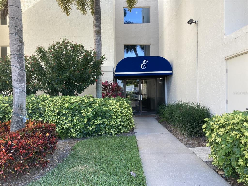 A concrete walkway leads to a building entrance marked with a blue awning labeled E — 6114 43RD STREET W UNIT 103E, BRADENTON, FL