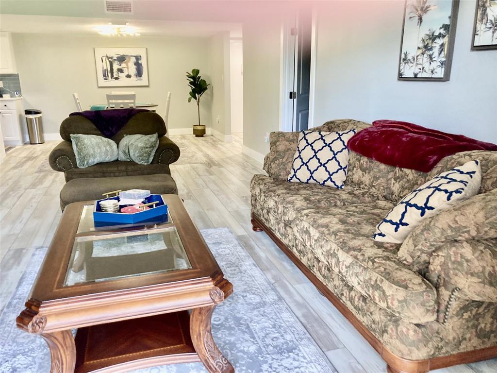 A living room features a floral sofa, a glass-topped coffee table, and wood-look flooring — 6114 43RD STREET W UNIT 103E, BRADENTON, FL