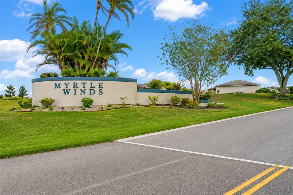 A curved community entrance sign for Myrtle Winds stands beside a paved road and lawn — 245 WINTER RIDGE BOULEVARD, WINTER HAVEN, FL