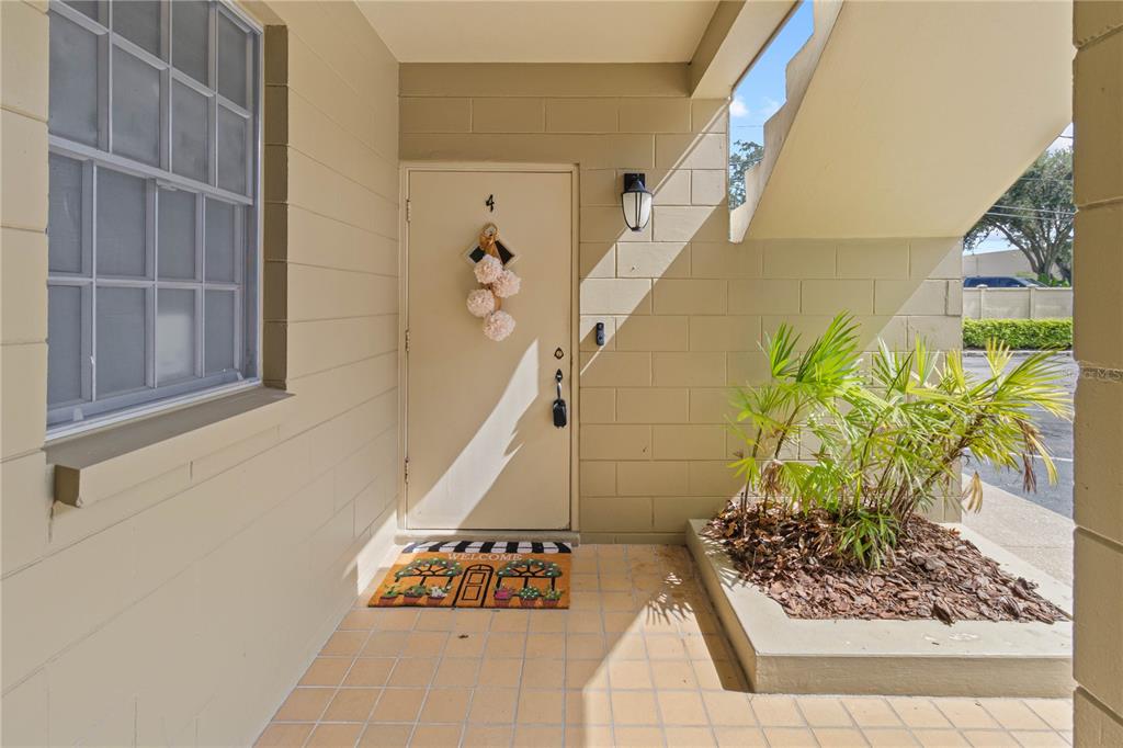 An exterior view of a building entrance featuring a tan door, a welcome mat, and landscaping — 223 WINDSOR STREET UNIT 4, LAKELAND, FL